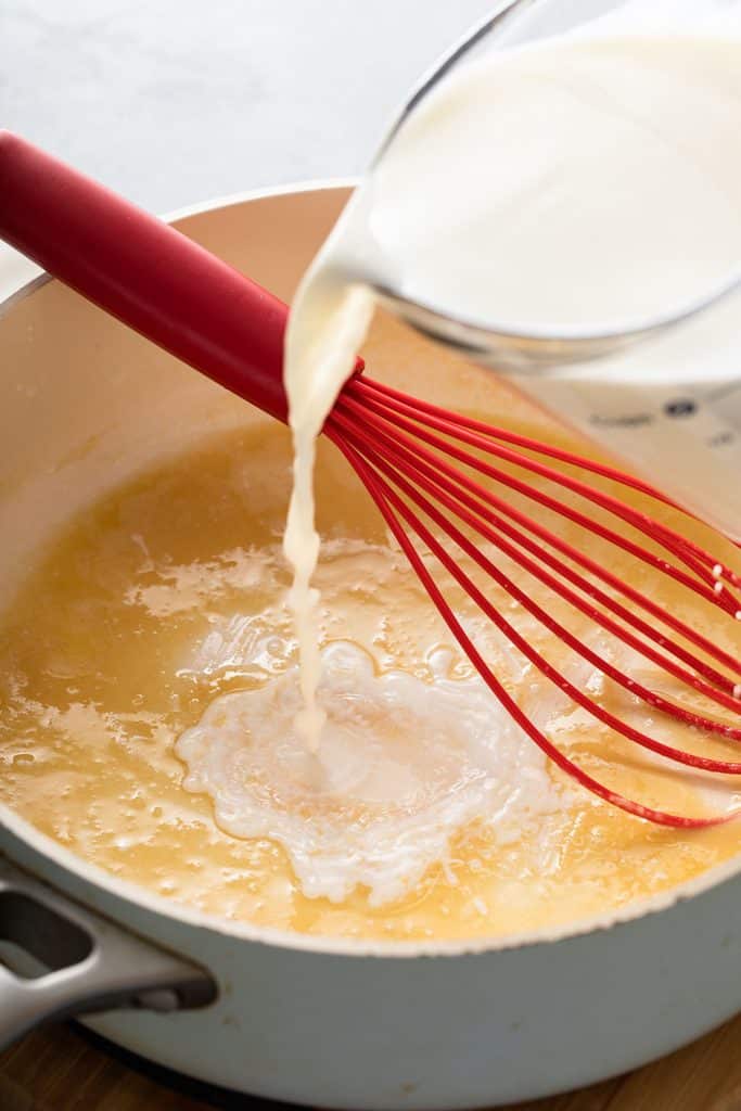 Pouring milk over a roux to make béchamel sauce.