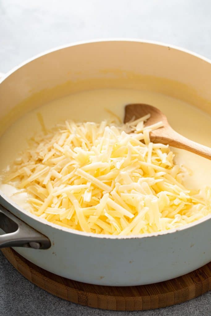 Shredded white cheddar cheese over white sauce in a saucepan