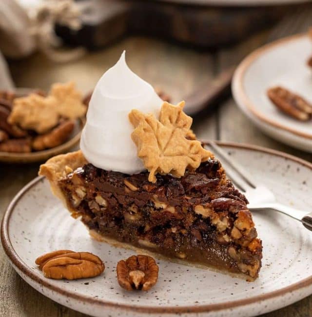 A piece of Chocolate Pecan pie topped with whipped cream and a leaf made of pie crust.