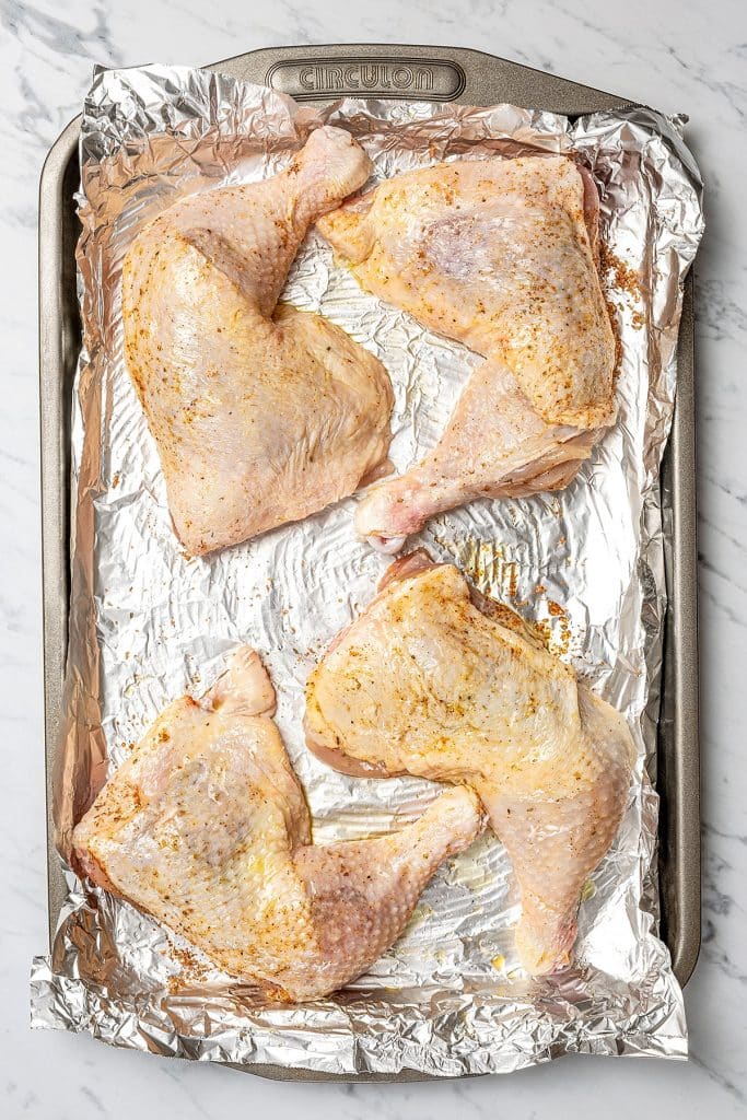 four seasoned chicken leg quarters on a prepared baking sheet