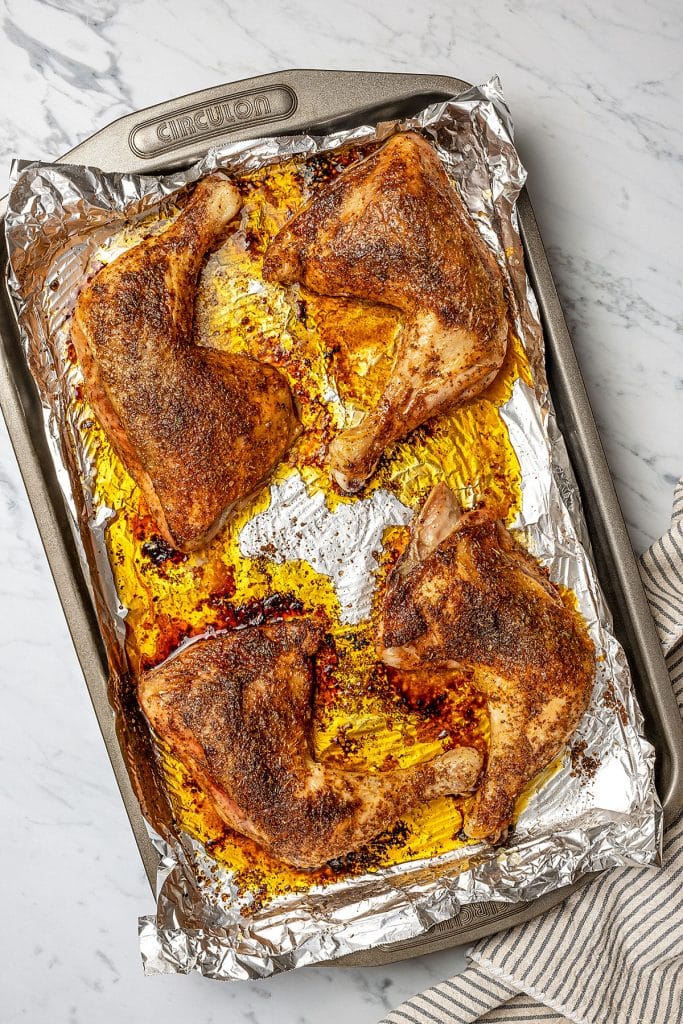 four juicy baked chicken leg quarters on a baking sheet with foil