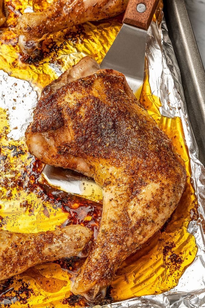 Taking a baked chicken leg quarter from a tray with a spatula.