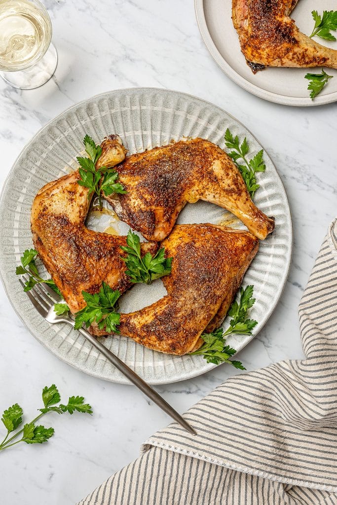 three baked chicken quarters on a gray plate garnished with cilantro