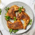 three baked chicken leg quarters on a gray plate garnished with cilantro