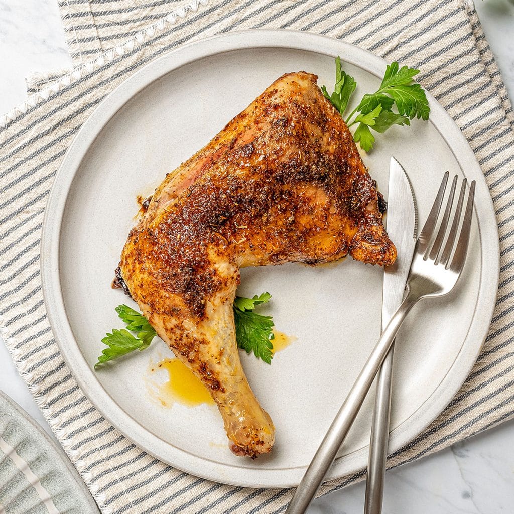 a leg quarter on a gray plate with a knife and fork 