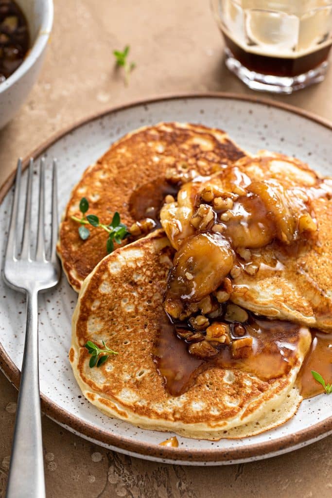 three fluffy pancakes topped with caramelized bananas and chopped pecans.