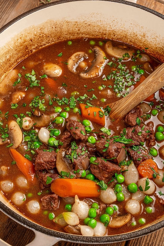 Beef stew with carrots,  pearl onions, peas and mushrooms in a Dutch oven