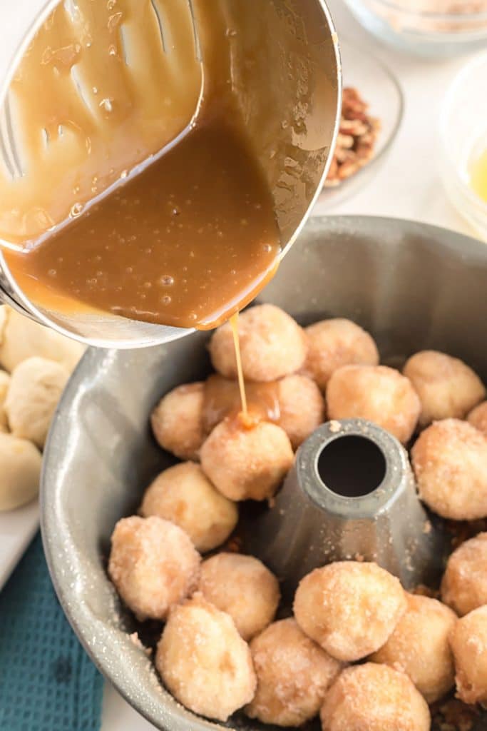 pouring caramel sauce over a bundt pan filled with sugared monkey bread dough balls