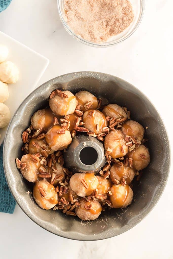 monkey bread dough balls in a bundt pan with caramel sauce and chopped pecans