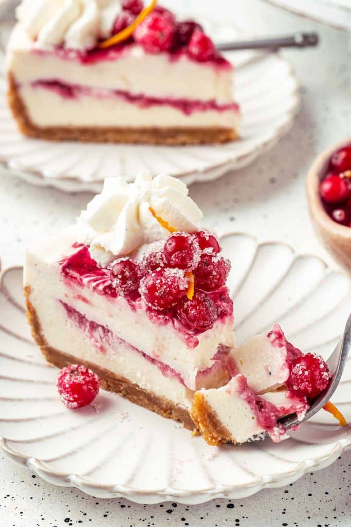 Slice of cranberry cheesecake topped with whipped cream and sugared cranberries