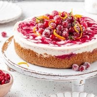 A whole cranberry cheesecake topped with sugared cranberries on a platter