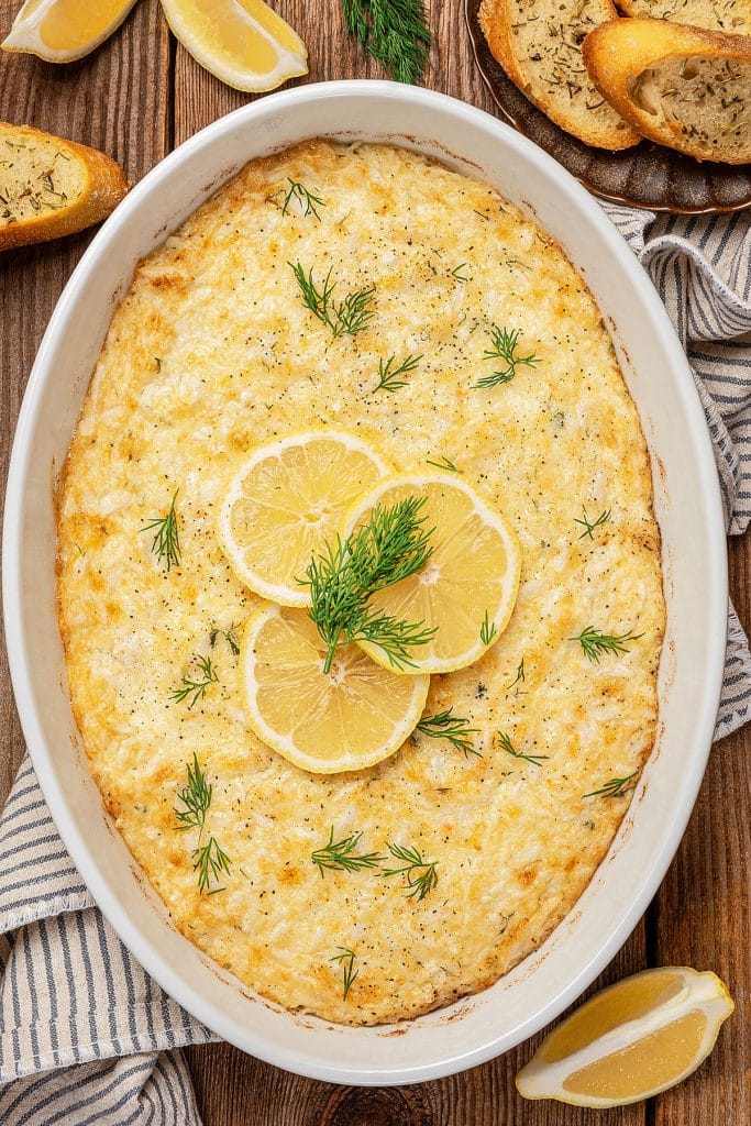 Top view of golden brown baked crab dip topped with thin lemon slices.