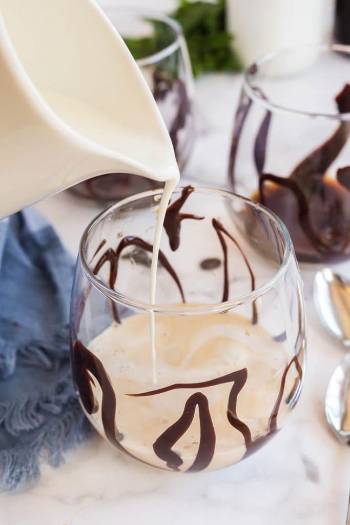 pouring half and half to a Chocolate drizzled glass with kahlua and condensed milk.