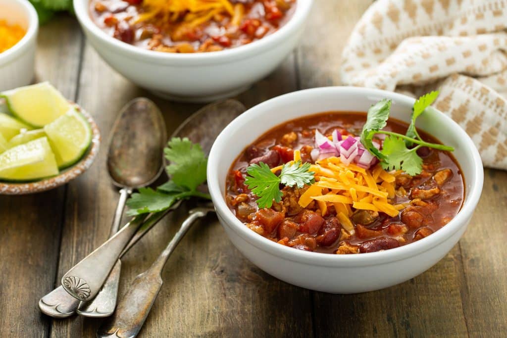 a bowl of healthy chili topped with chopped red onion, shredded cheddar cheese and cilantro