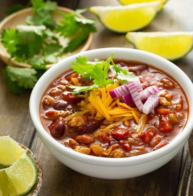 Turkey chili in a white bowl garnished with chopped red onion, shredded cheese and cilantro