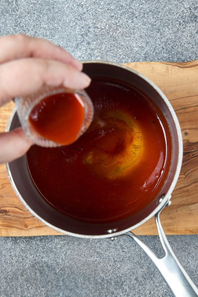 pouring hot sauce into a saucepan with bbq sauce.