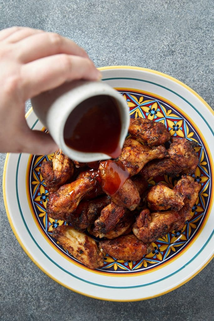 pouring bbq sauce over crispy golden brown chicken wings