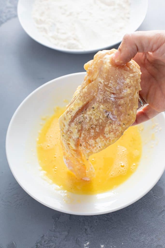 A piece of chicken dredged in flour is getting dipped into egg