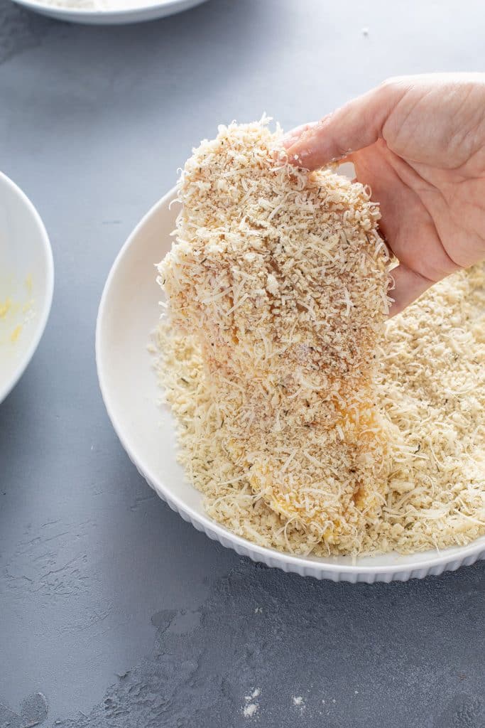 Breaded chicken cutlet getting lift from a plate with panko breadcrumbs