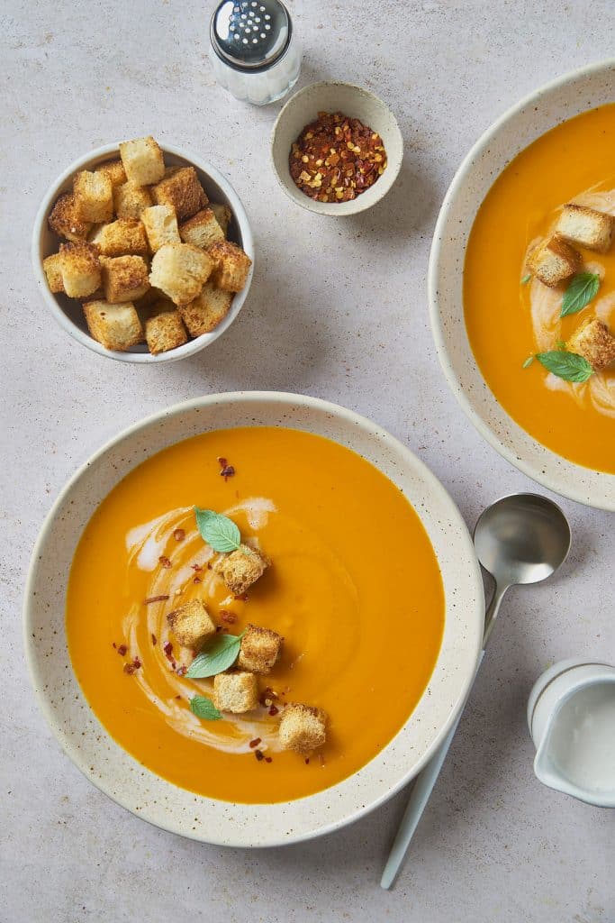 Bowls of creamy and velvety carrot soup with crouton toppings and coconut milk drizzle.
