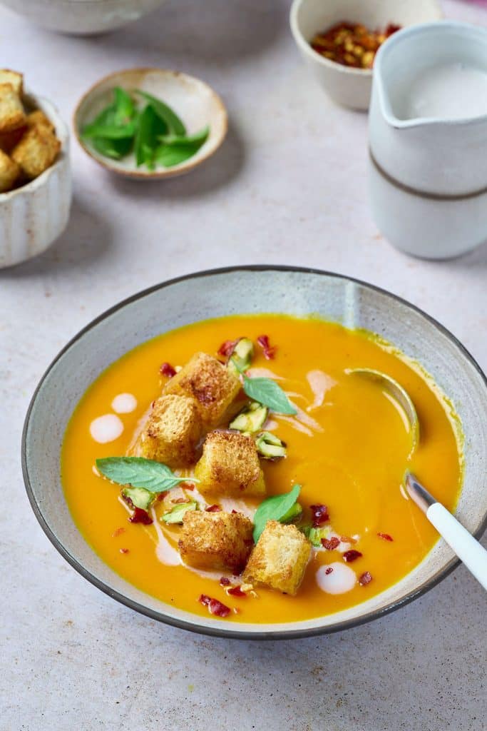 A bowl of vegan carrot soup with crouton, fresh herbs and coconut milk drizzle