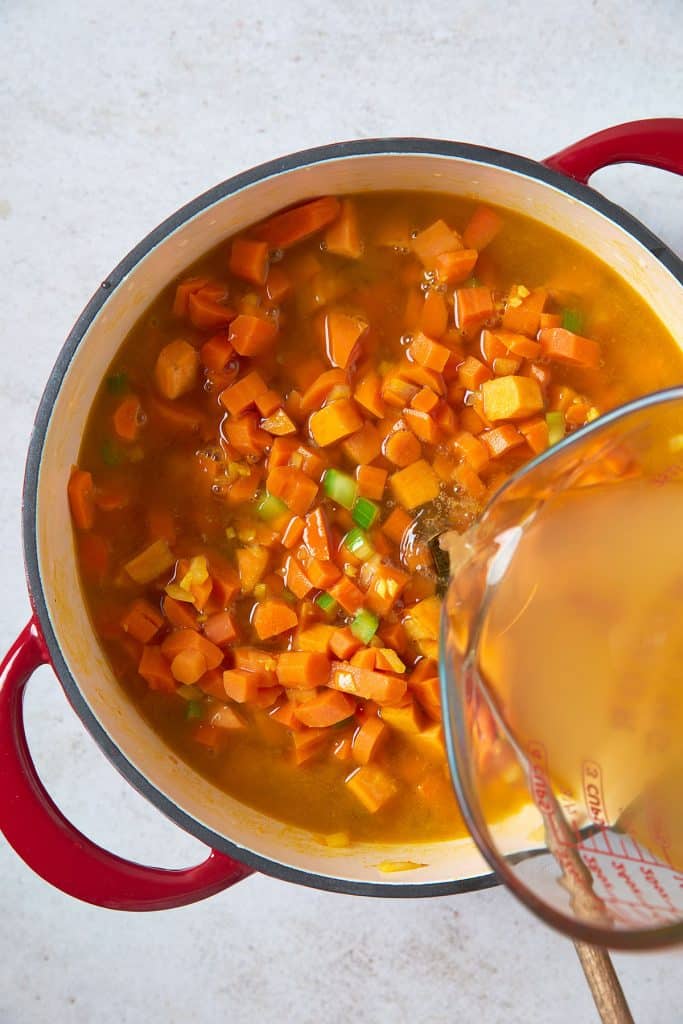 Pouring veggie broth over cooked vegetables in a soup pot