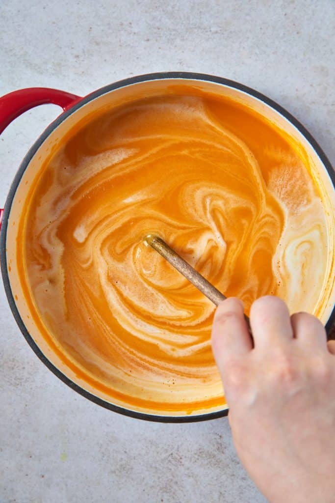 Stirring coconut milk into vegan carrot soup.