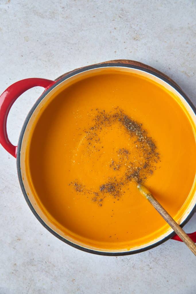 Creamy and smooth vegan carrot soup in a pot sprinkled with black pepper.