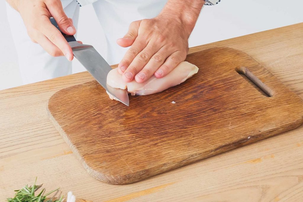 Slicing raw chicken breasts in half lengthwise.