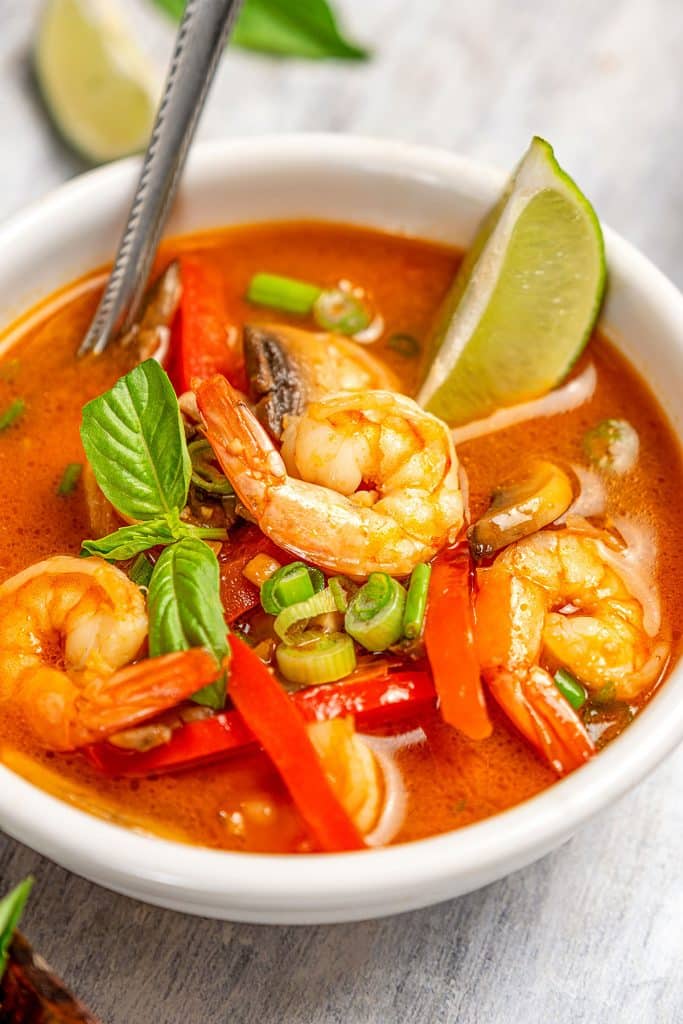 Close up view of a bowl of Thai coconut curry soup with large shrimp in a white bowl.