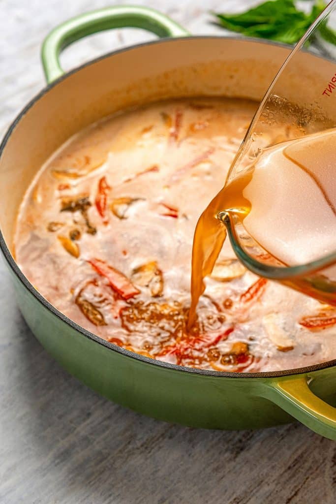 Broth been added to a Dutch oven with sautéed veggies and red curry paste.