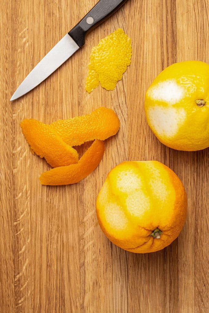 an oranges and a lemon partially peeled on a wooden board