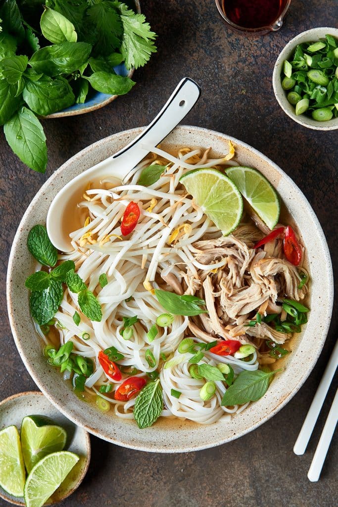 top view of a bowl full with chicken, rice noodles and lots of fresh herbs in the most flavorful, rich broth.