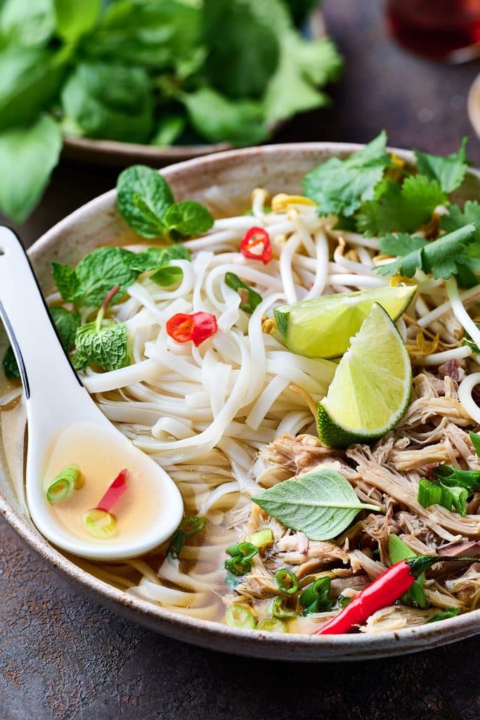 A big bowl of instant pot pho topped with bean sprouts, herbs and slices of lime.