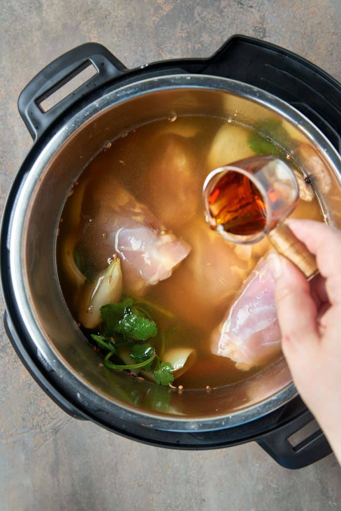 adding fish sauce to the chicken and other ingredients that are simmering in chicken broth in the instant pot