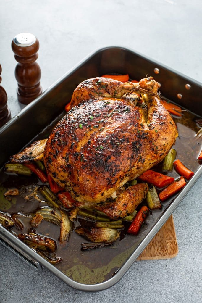 top view of a whole roasted chicken in a roasting pan with vegetables and their juices