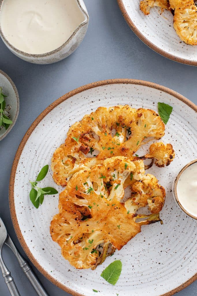 Golden brown and crispy on the ages cauliflower steaks served on a plate
