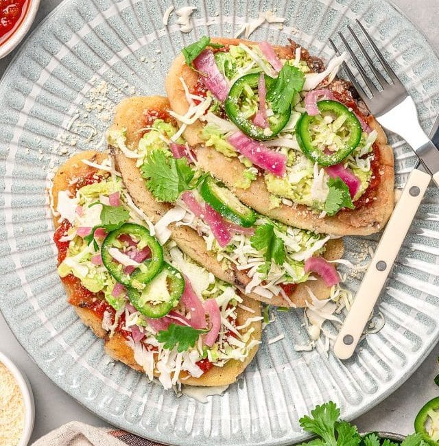 Three tlacoyos with toppings served on a plate