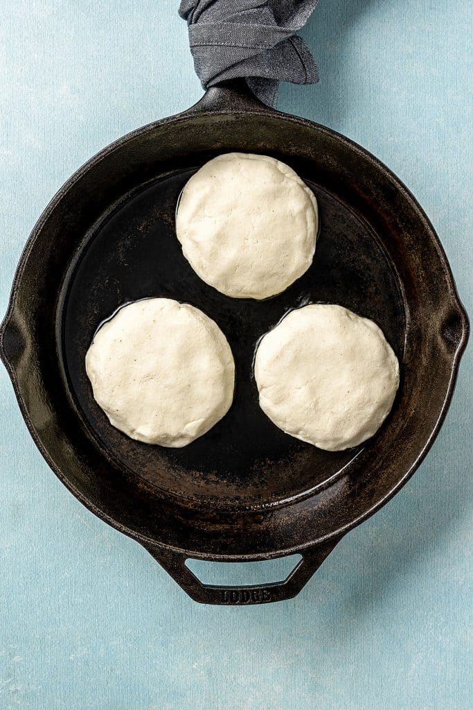 three arepas con queso cooking on a large skillet with butter