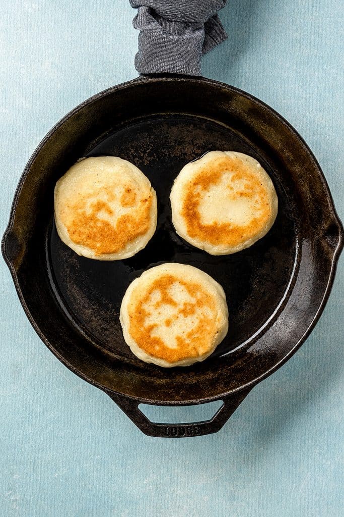 three golden brown cheese arepas on a skillet