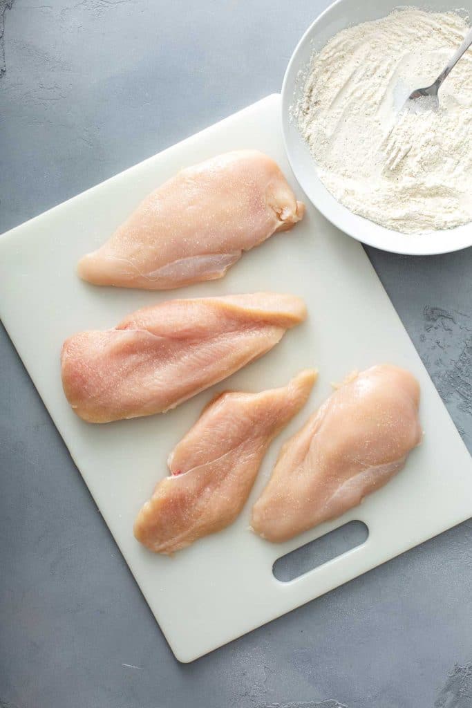 two chicken breasts cut in half lengthwise over a white cutting board