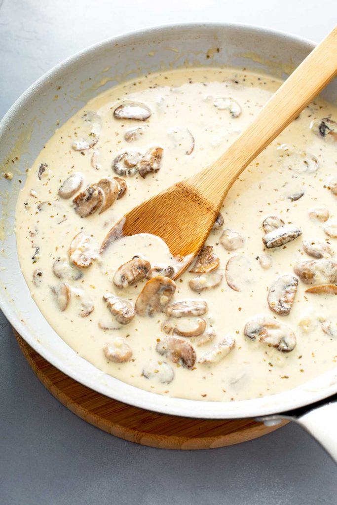 mushrooms with heavy cream on a skillet with a wooden spoon
