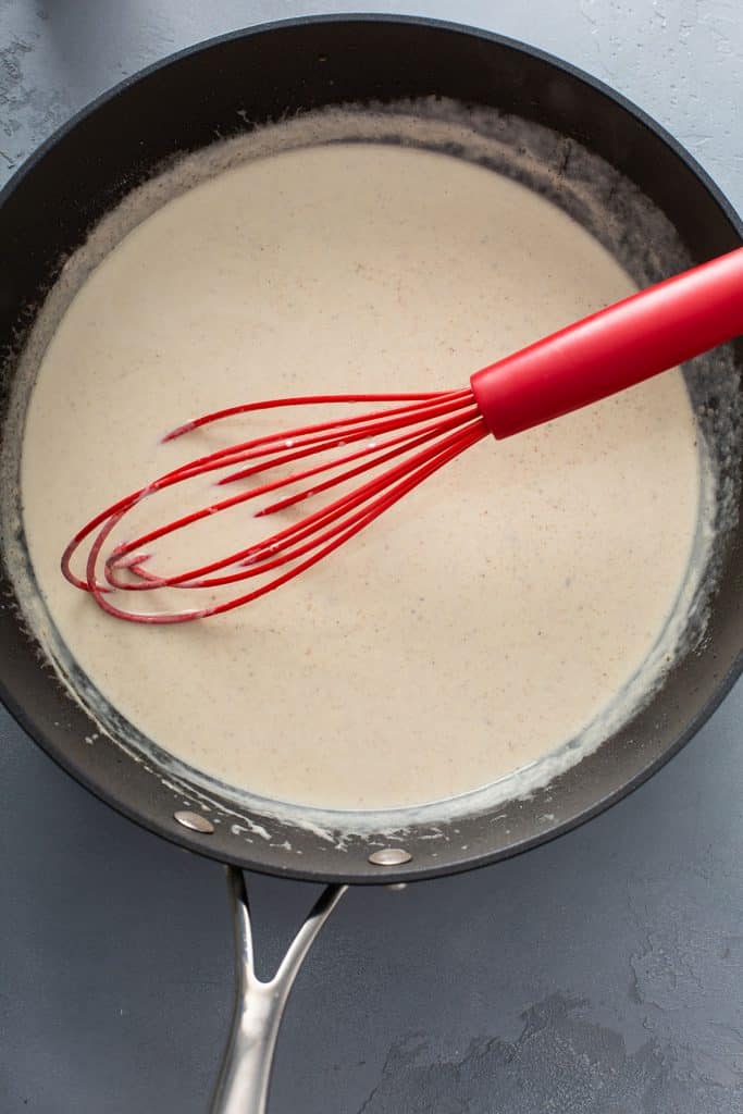 lemon creamy sauce in a skillet with a red whisk.