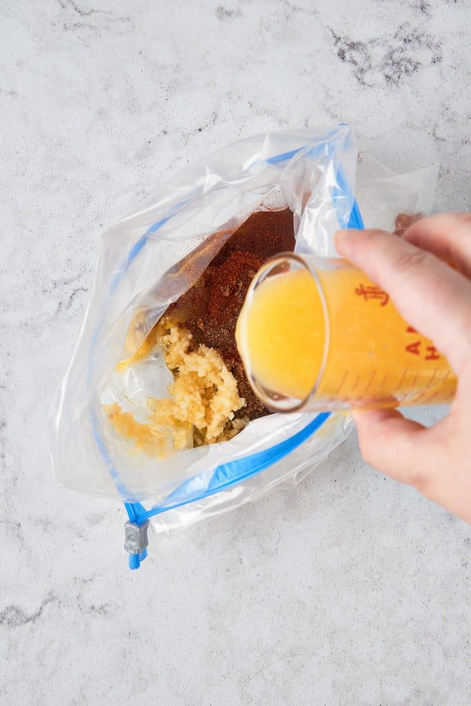 Adding fresh orange juice into a resealable bag with spices