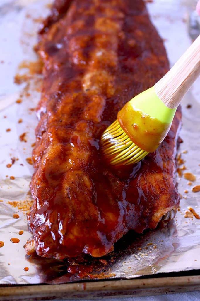 Cooked ribs are brushed with BBQ sauce