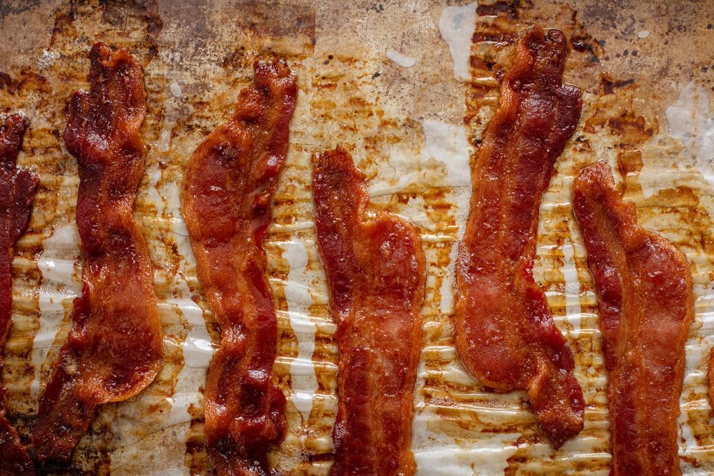 Cooked crisp bacon on a parchment paper lined baking sheet pan.