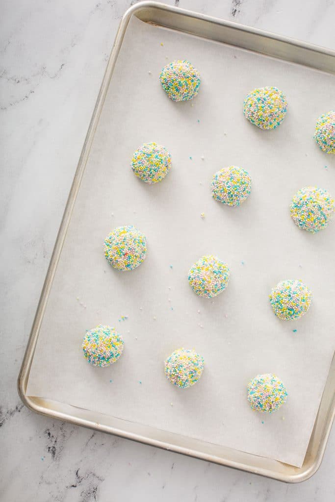 twelve funfetti cookie dough balls lined up on a baking tray