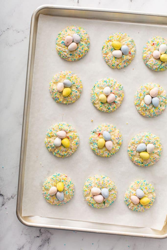 twelve funfetti cookies decorated with chocolate easter eggs and sprinkles on a baking tray