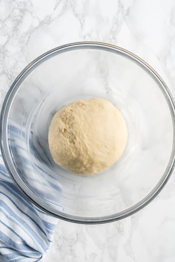 the bun dough shaped into a ball in a clear bowl