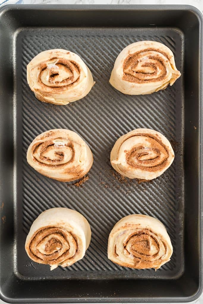 six cinnamon roll dough pieces in a baking tray